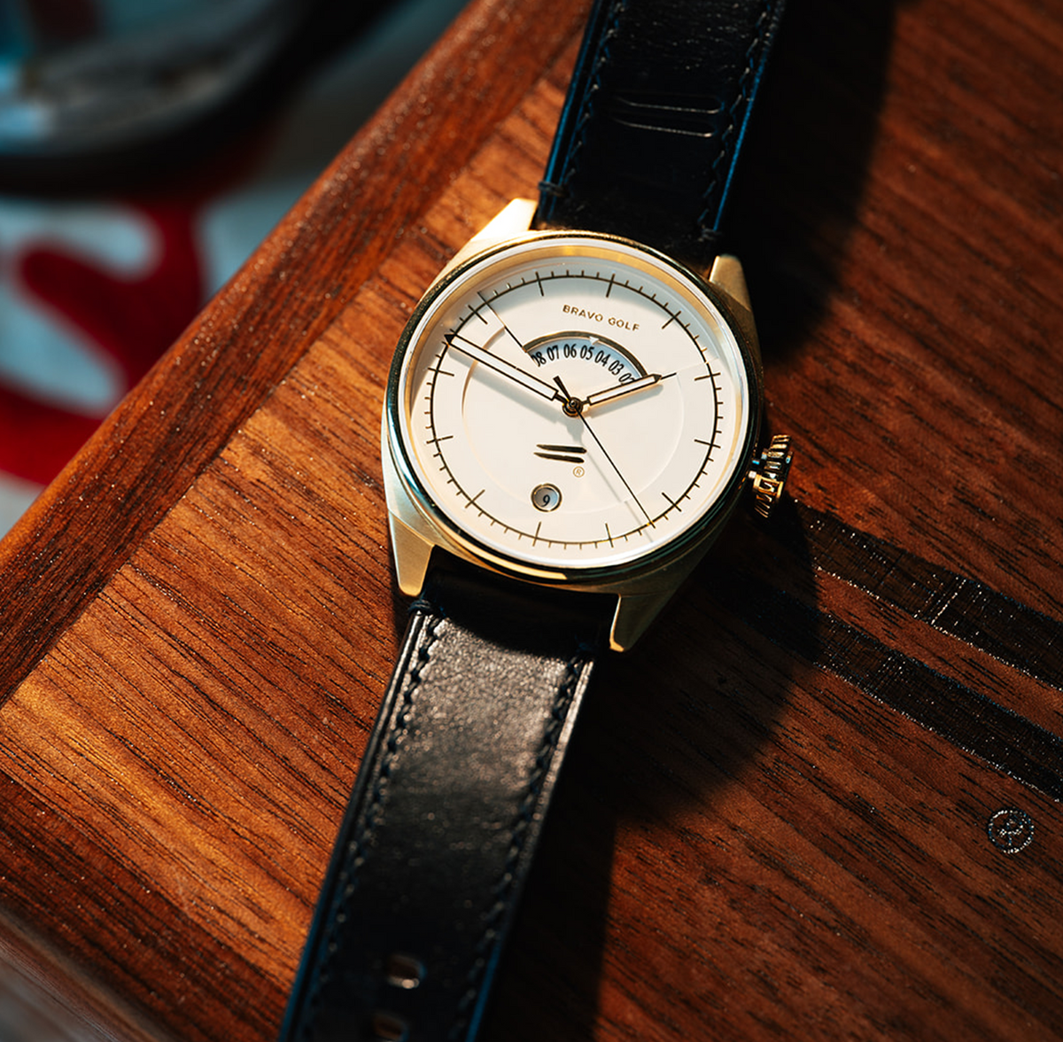 The Bishop watch with a white dial and dark leather strap on a wooden surface.
