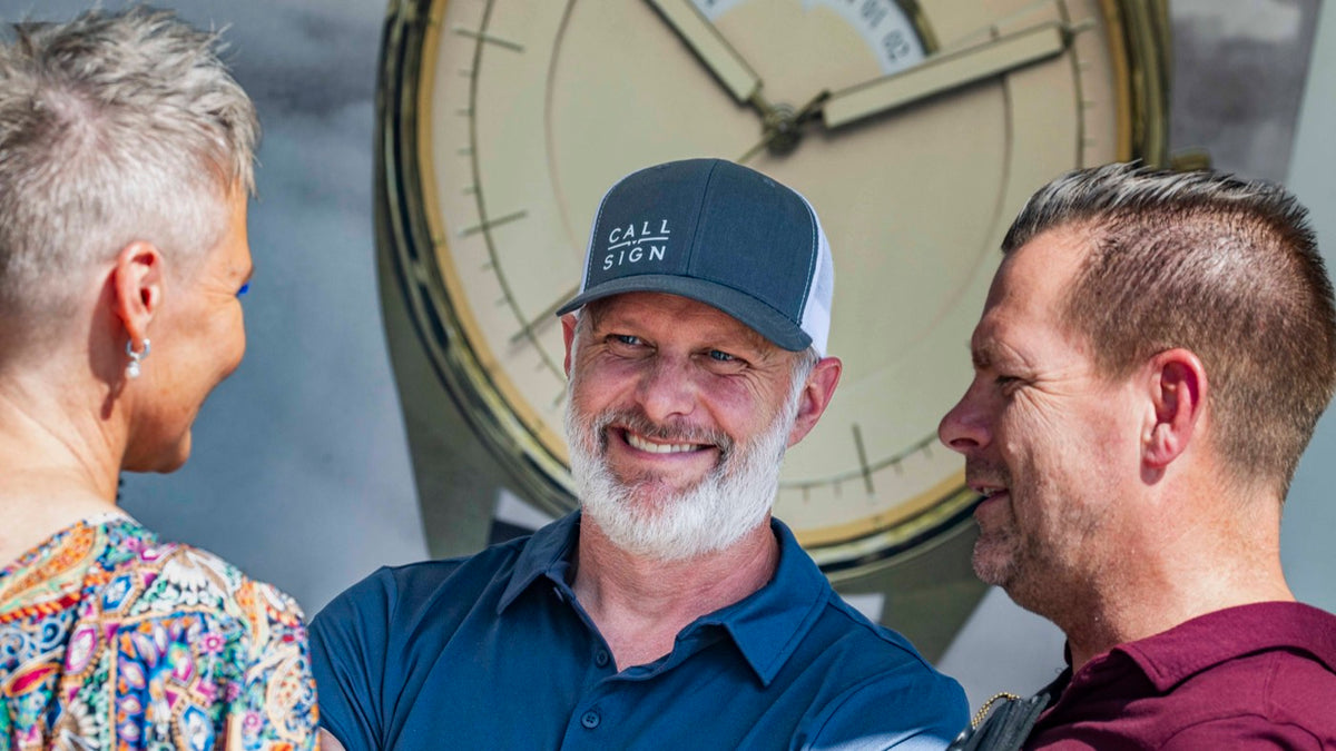 Beau Garrett, in a Call Sign cap, laughing with two visitors at the Call Sign booth at the Pacific Airshow.