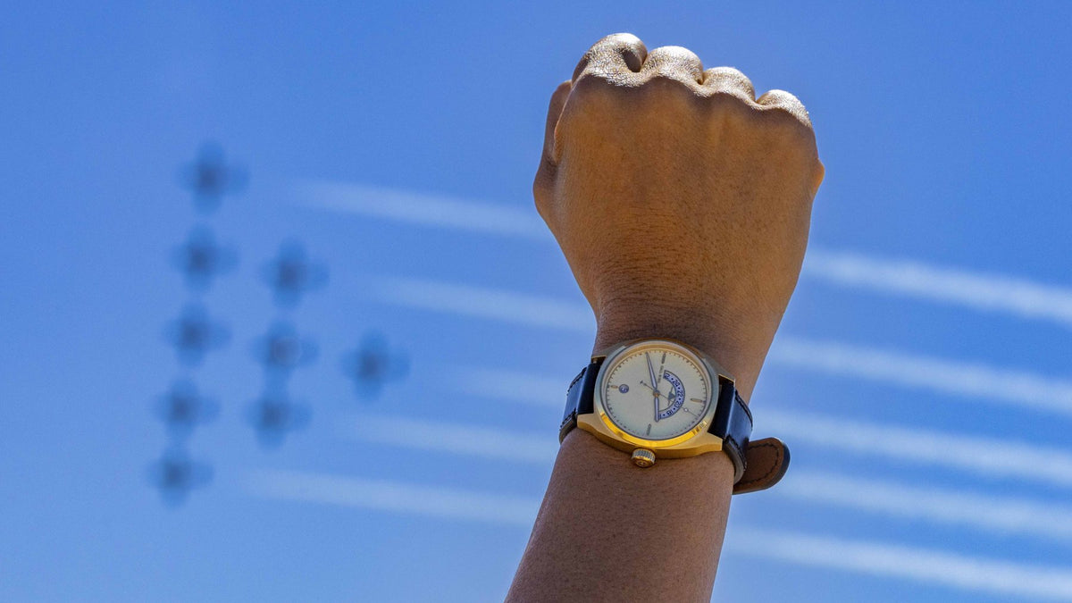 A raised wrist wearing a Discovery with jets trailing smoke in the sky.