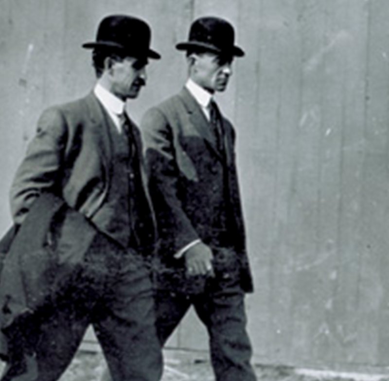 Archival photograph of Wilbur and Orville Wright standing side by side in suits and bowler hats.