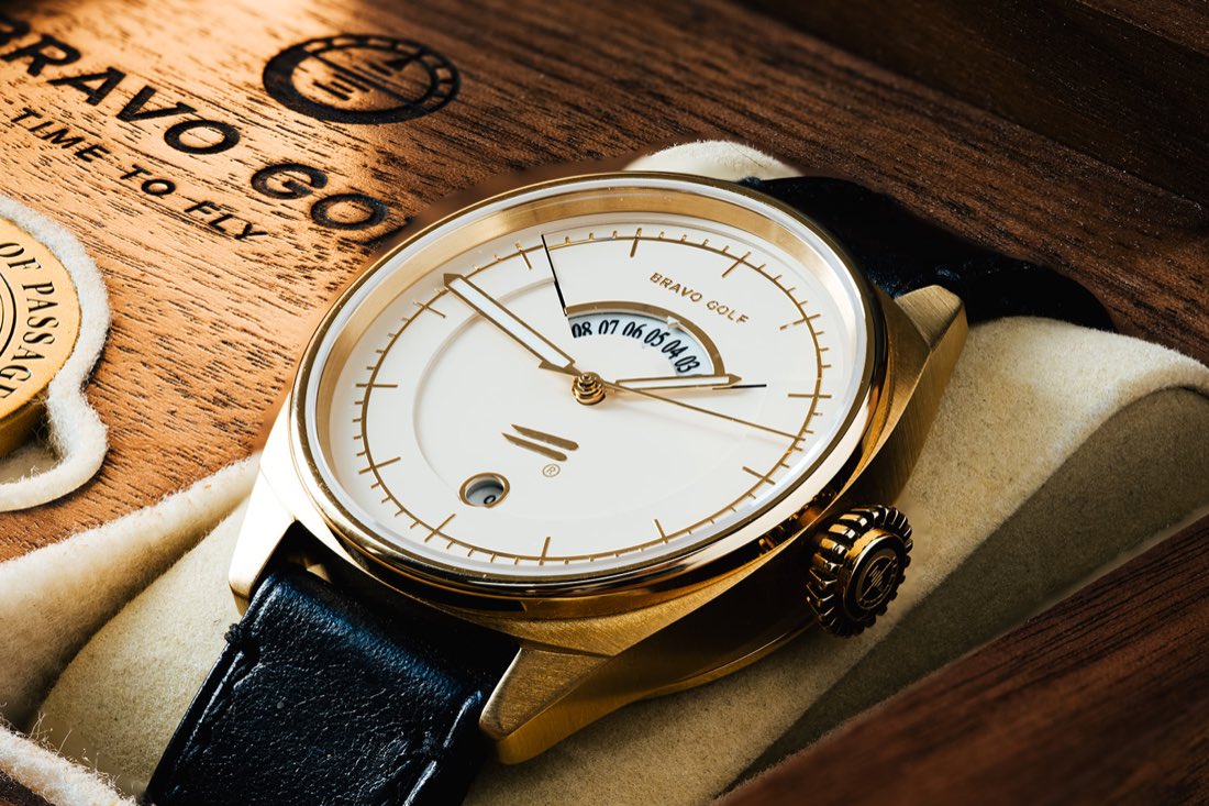 The Bishop resting in its walnut presentation box: cream dial, gold-tone case and crown, crescent GMT window at 12, black leather strap.